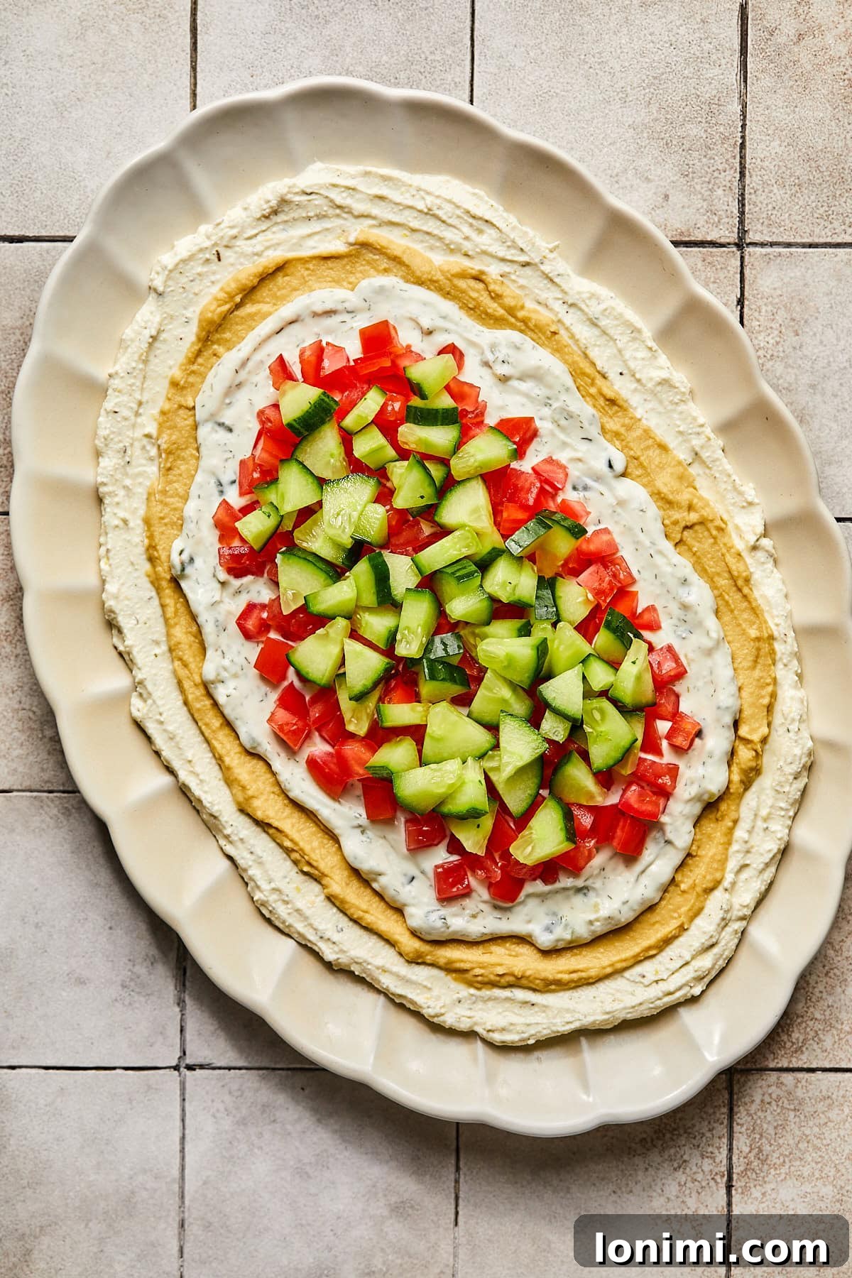 Effortless Mediterranean Layered Feta Dip 8 whipped feta with hummus and tzatziki topped with tomatoes and cucumbers