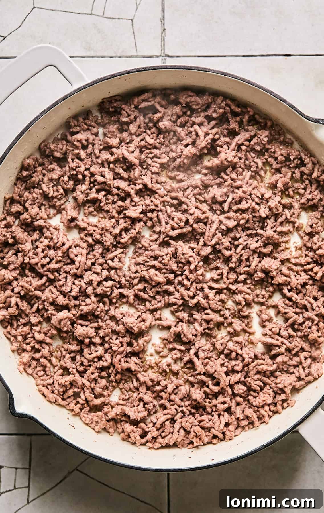 Ground beef cooking and browning in a large skillet, ready for the next steps.