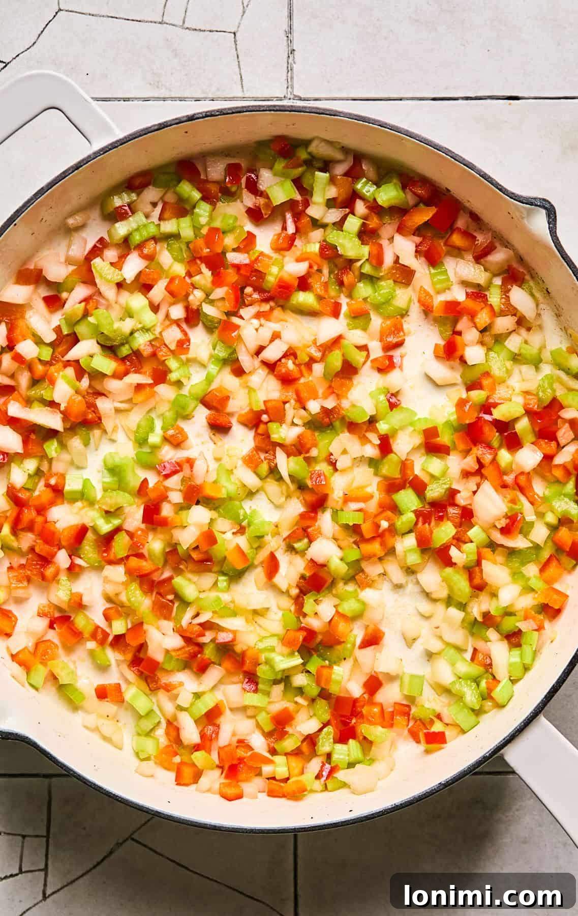 A vibrant mix of onions, celery, bell pepper, and garlic sautéing in a skillet, releasing their aromatic flavors.