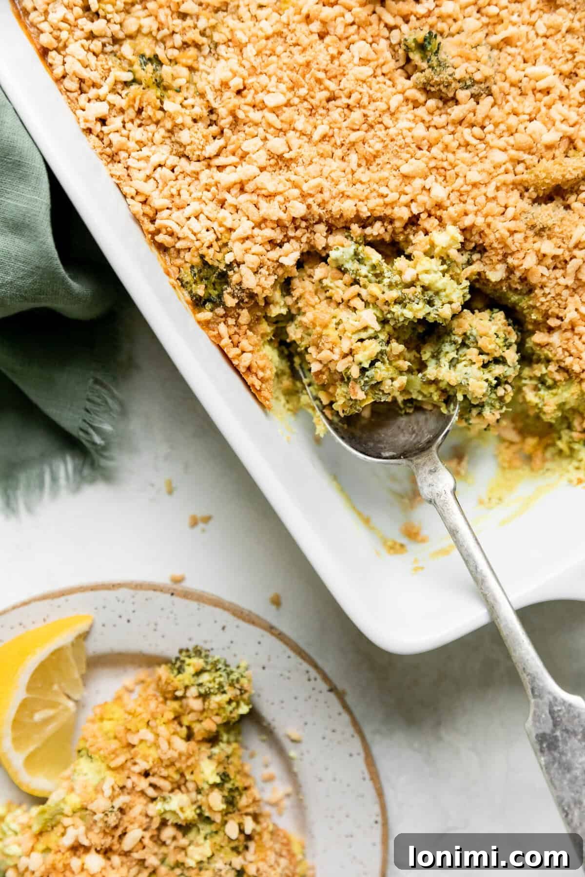 vegan broccoli casserole in a white dish with a spoonful scooped out with a silver spoon and a plate on the side