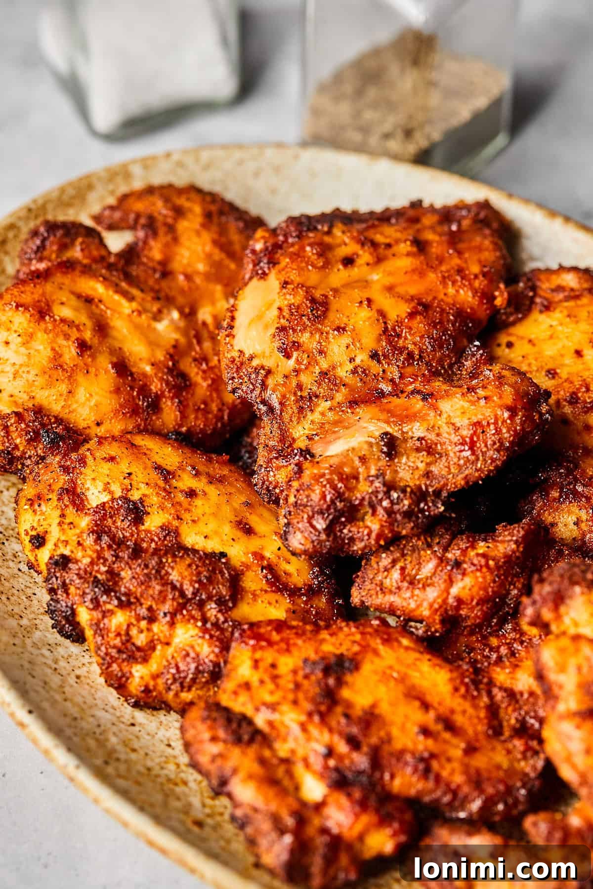 Air fryer boneless chicken thighs artfully arranged on a pristine white plate, garnished with fresh herbs and a lemon wedge, showcasing their golden-brown, crispy exterior and succulent texture.