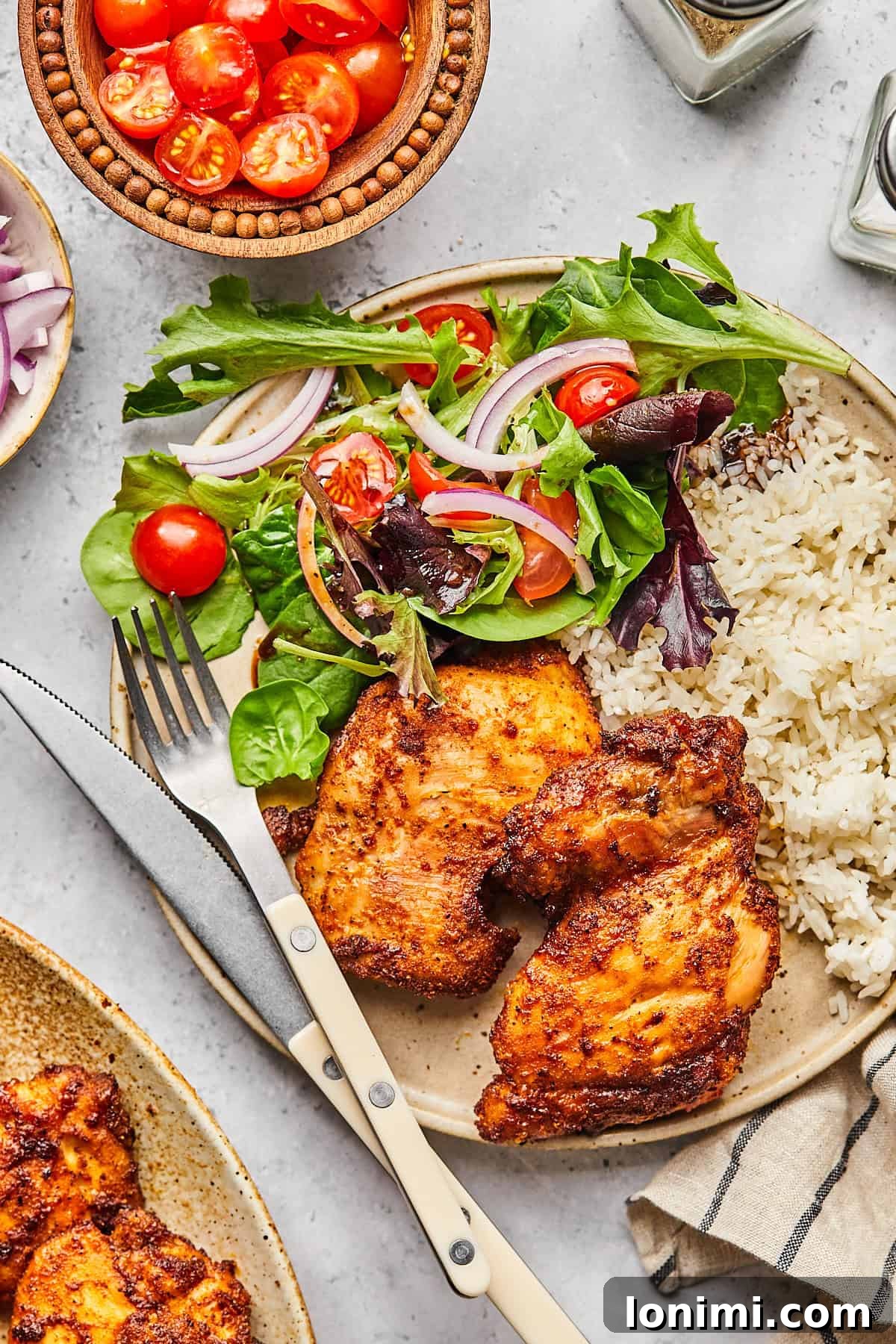 A beautifully plated meal featuring golden-brown air fryer boneless chicken thighs, served alongside fluffy white rice and a fresh green salad, highlighting a balanced and appealing presentation.