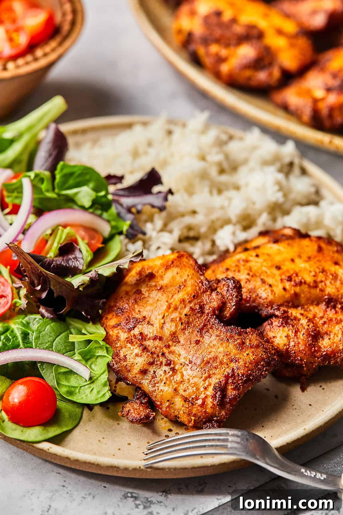 A rustic plate showcases a perfectly cooked air fryer boneless chicken thigh, served alongside fluffy rice and a crisp green salad, with a fork poised for a delicious bite.