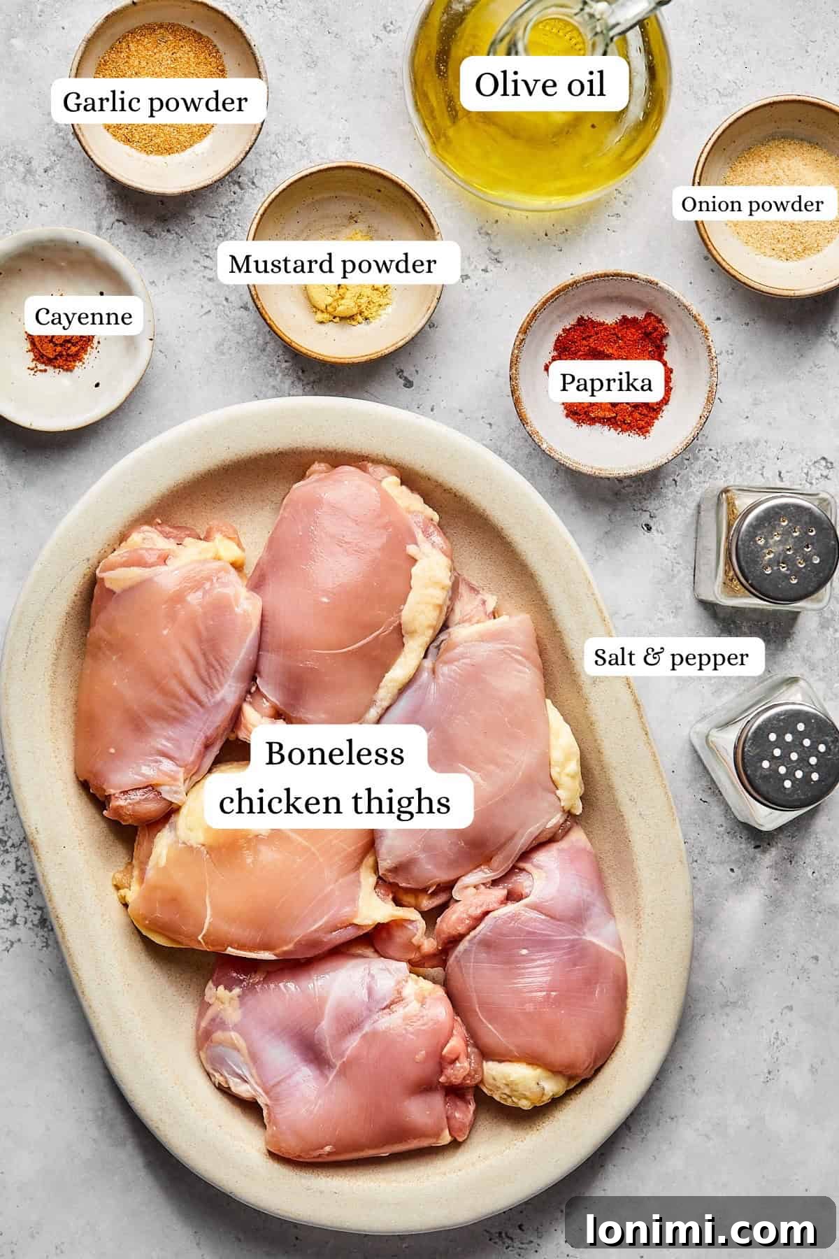 A collection of small white bowls meticulously labeled with the names of various spices—salt, pepper, garlic powder, onion powder, paprika, dry mustard powder, and cayenne pepper—arranged around a central bowl of glistening olive oil, all set against a rustic wooden background.