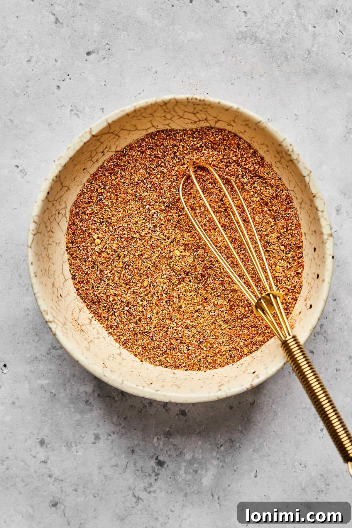 A small, elegant white bowl holds a meticulously blended mix of aromatic spices, creating a rich, earthy brown powder ready to season the chicken.
