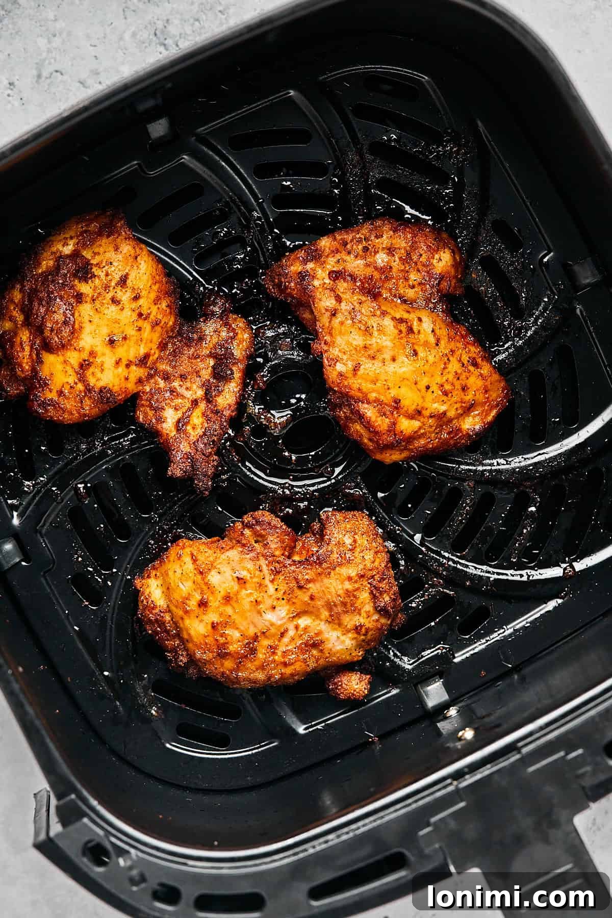 Perfectly cooked, golden-brown air fryer chicken thighs, showcasing their crispy skin and juicy interior, rest in the air fryer basket after cooking.