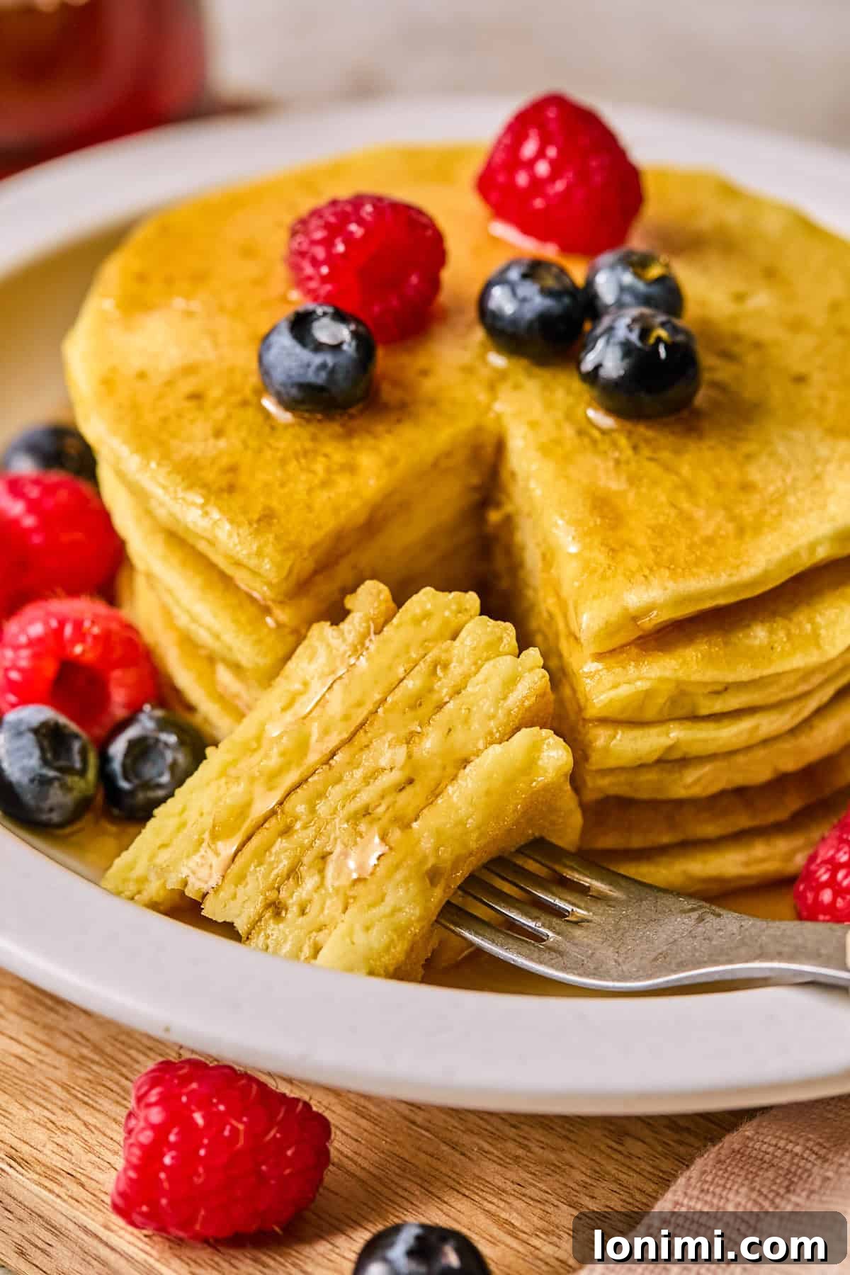 Ultimate Cottage Cheese Protein Pancakes 2 A fork holding a bite of fluffy cottage cheese protein pancake, drizzled with maple syrup and garnished with fresh berries.