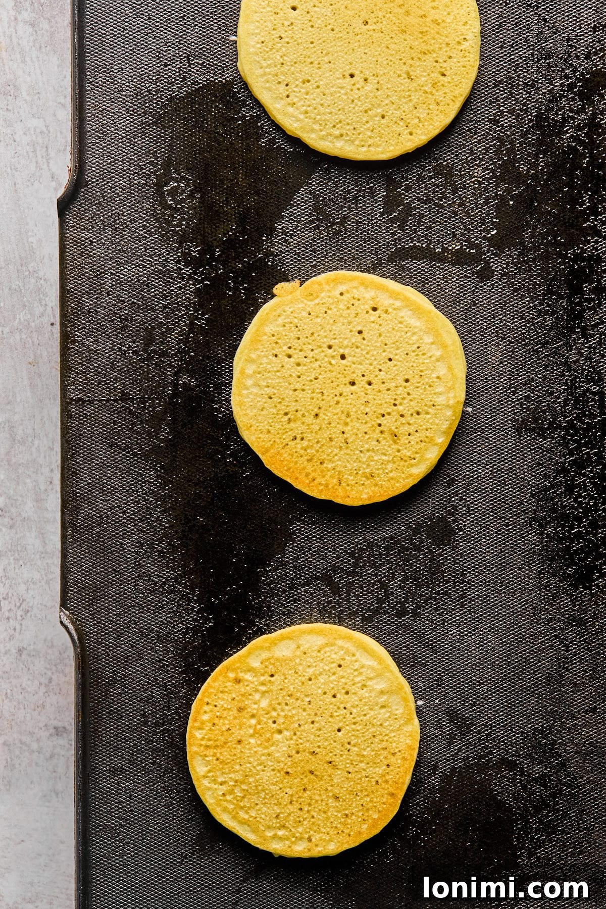 Ultimate Cottage Cheese Protein Pancakes 7 A pancake being flipped on a griddle, revealing a perfectly golden-brown cooked side, while the uncooked side is still visible.