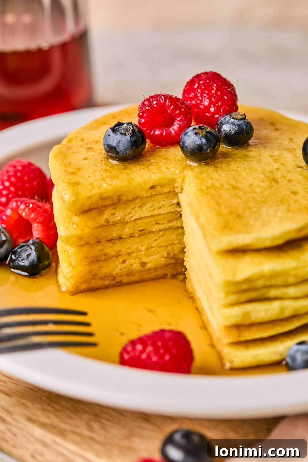Ultimate Cottage Cheese Protein Pancakes 9 Six fluffy protein pancakes stacked high on a white plate, with a large, inviting triangle bite taken out of the top pancake, showing its airy interior.