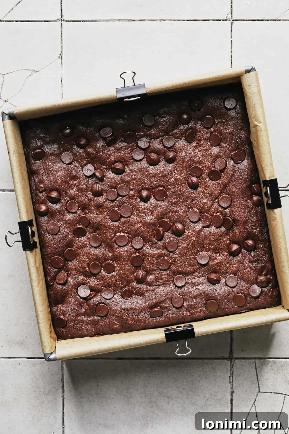 Rich Fudgy Protein Brownies With 7g Protein And A Clean Taste 10 protein brownies in a square baking pan lined with parchment paper and clips to hold the paper down.