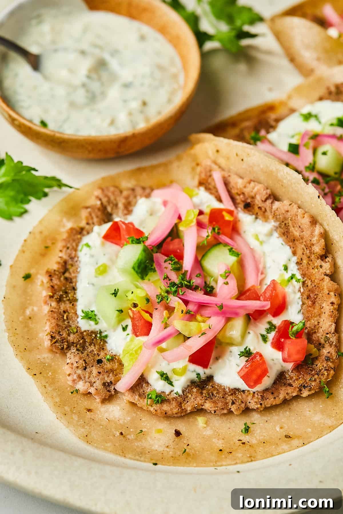 an open-faced smash burger topped with dill yogurt sauce, pickled onions, tomatoes and cucumbers
