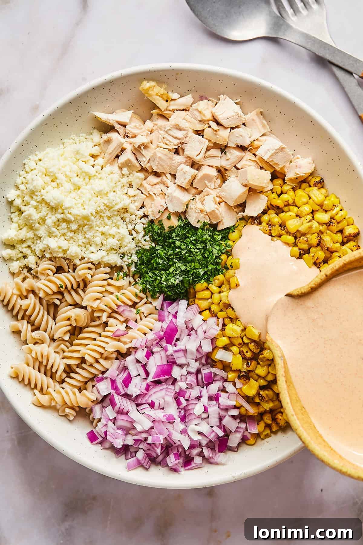 All the main ingredients for street corn pasta salad, including cooked pasta, corn, chicken, and onion, in a large bowl with dressing being poured over them.