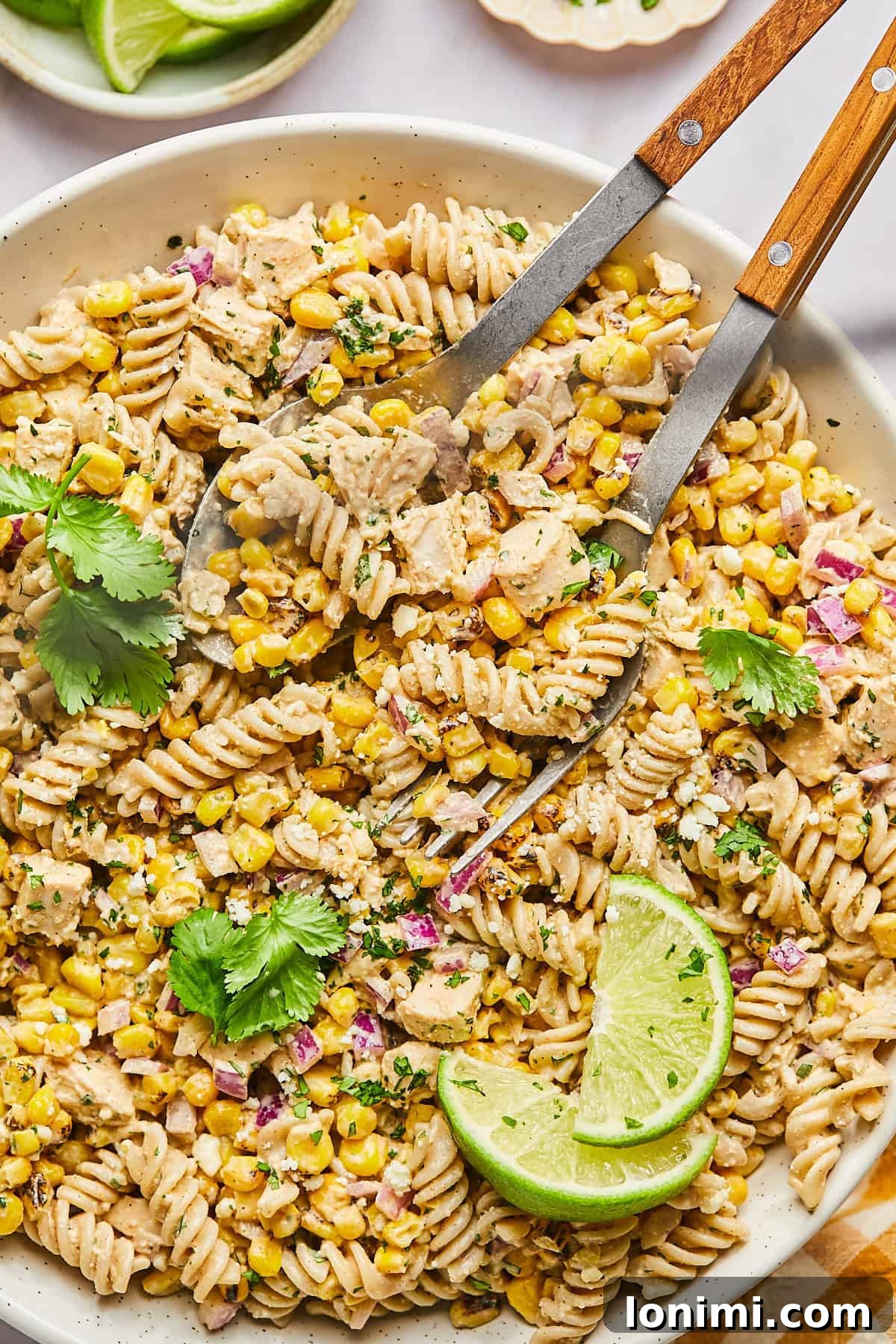 A large bowl of Mexican street corn pasta salad with serving tongs, ready to be enjoyed.