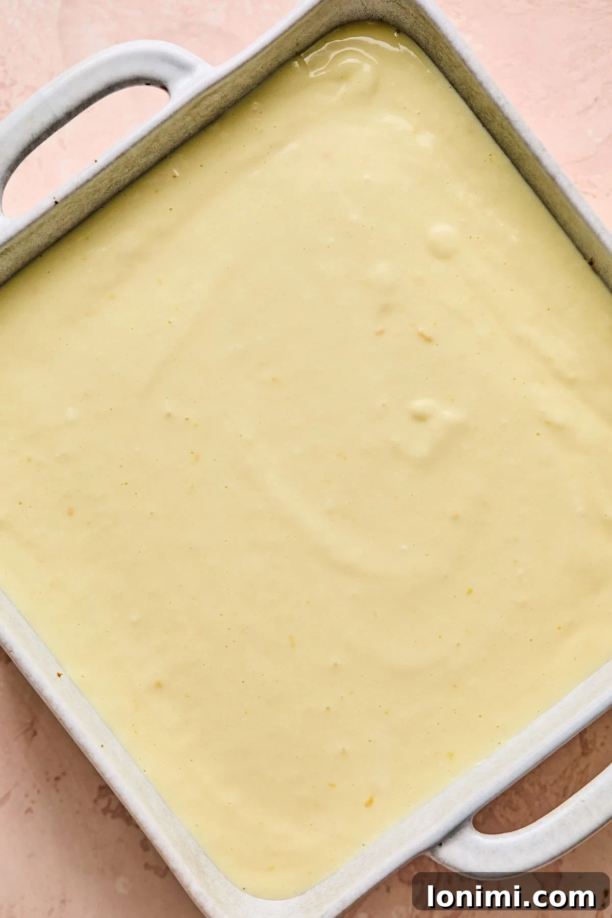 The smooth, creamy cheesecake filling freshly poured over the warm graham cracker crust in a white square baking pan, ready for the next step.