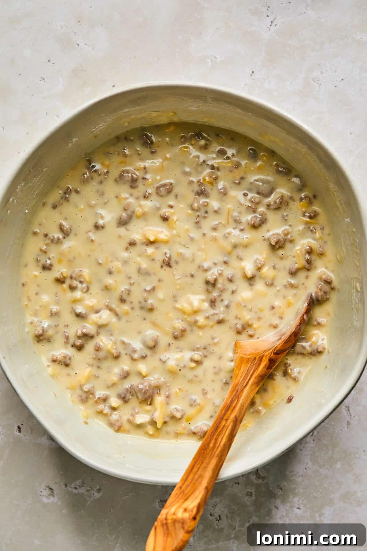 Mixing pancake batter with cheese, sausage, and maple syrup in a skillet