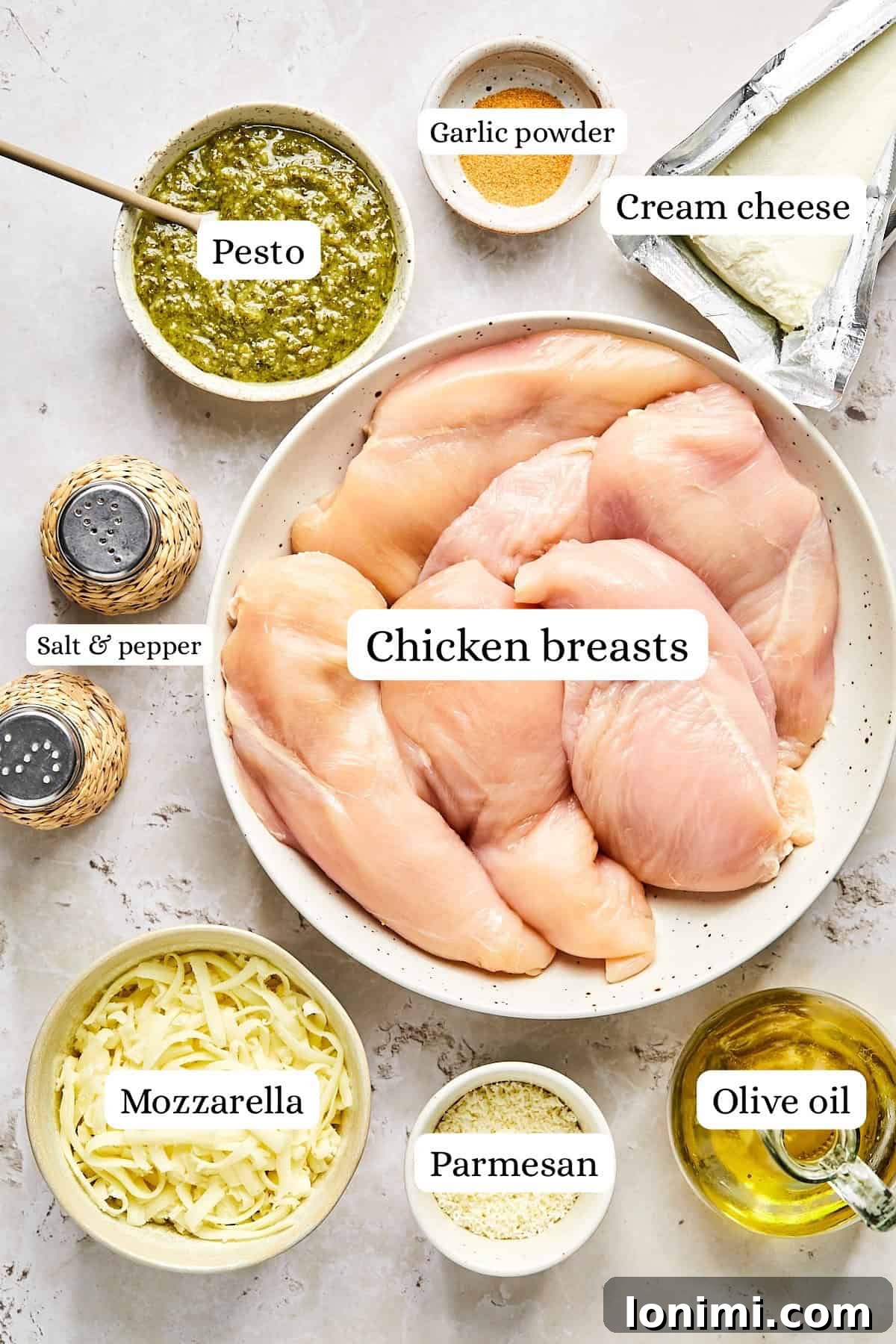 Ingredients for pesto chicken bake including chicken breasts, pesto, cheeses, and seasonings