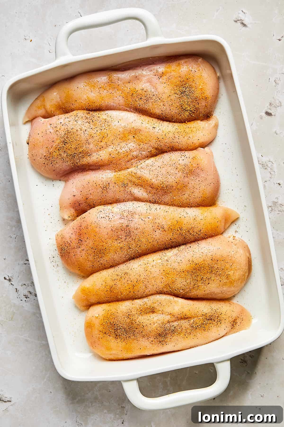 Raw chicken breasts seasoned in baking dish ready for pesto topping
