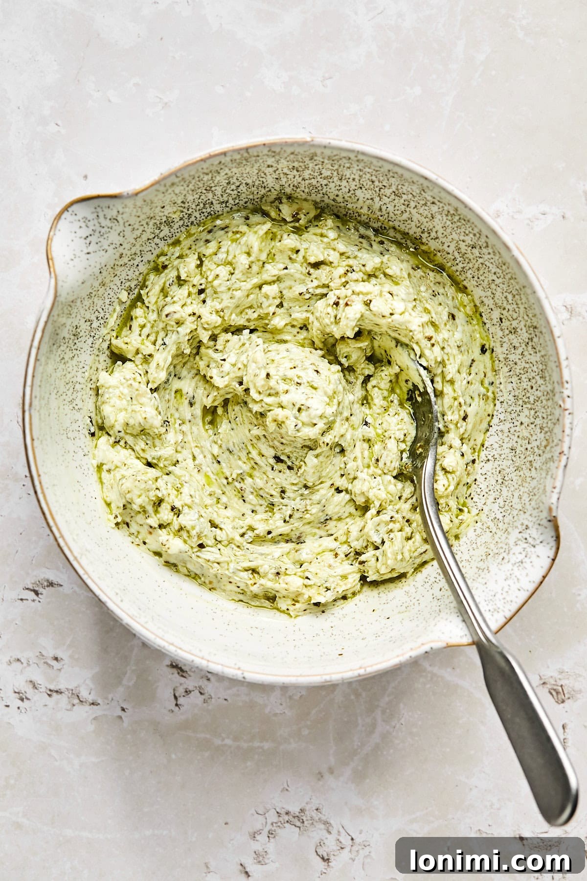 Cream cheese and pesto mixture being stirred in a bowl