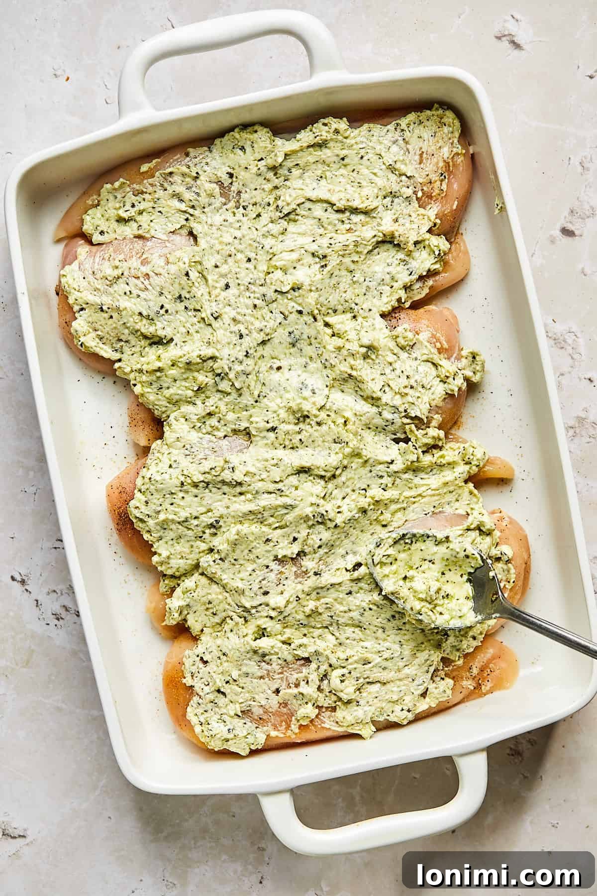Pesto cream cheese mixture spread over chicken in baking dish