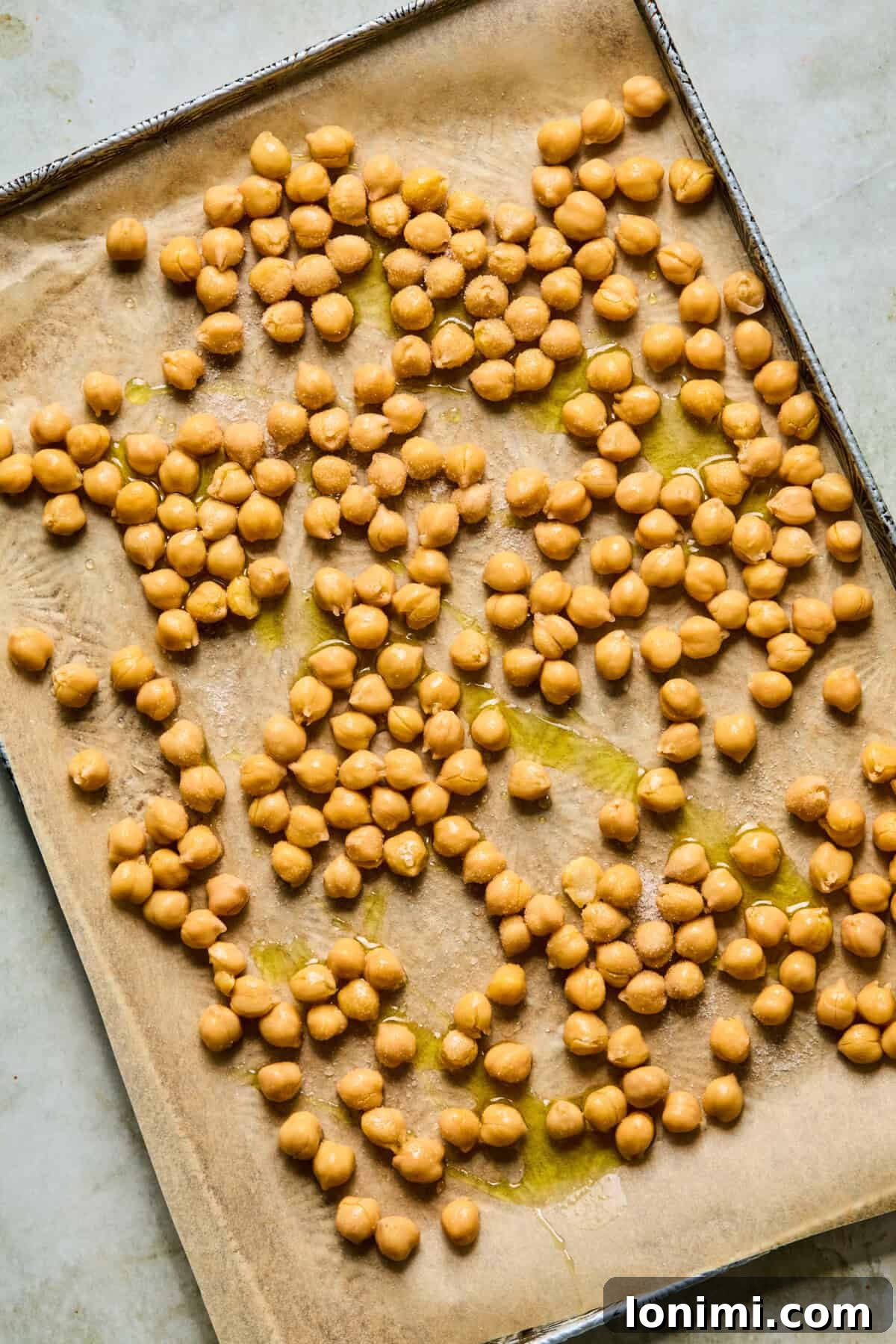 Step 1: Raw chickpeas spread evenly on a parchment-lined baking sheet, ready for roasting.