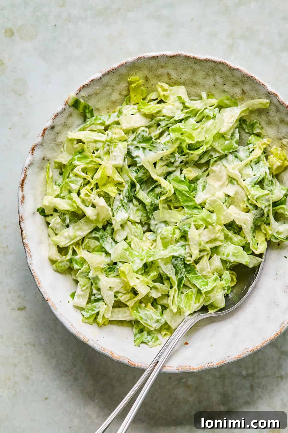 Step 7: Fresh romaine lettuce being tossed with creamy Caesar dressing in a clear glass bowl.