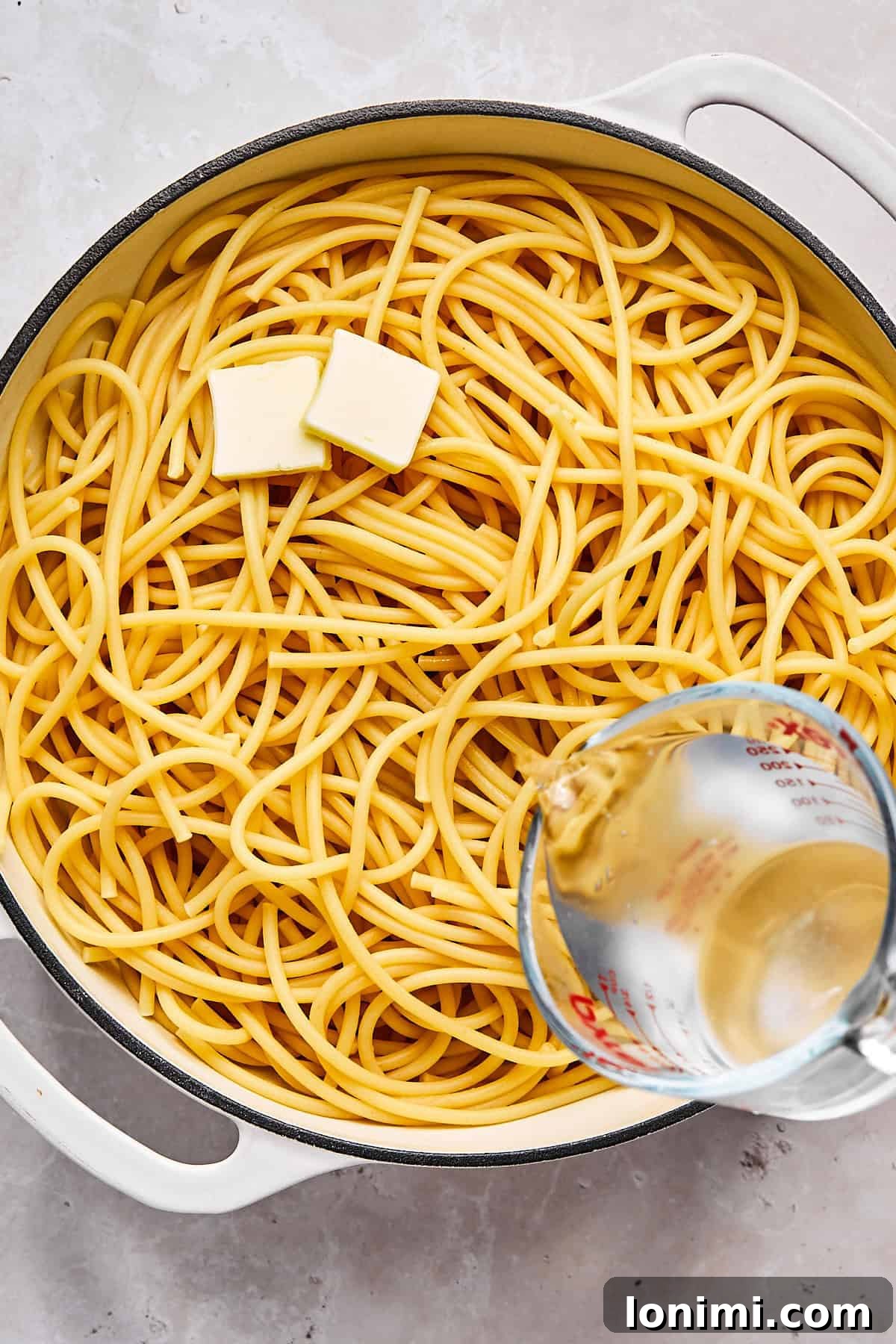 Cooked bucatini in a skillet with melted butter and reserved pasta water