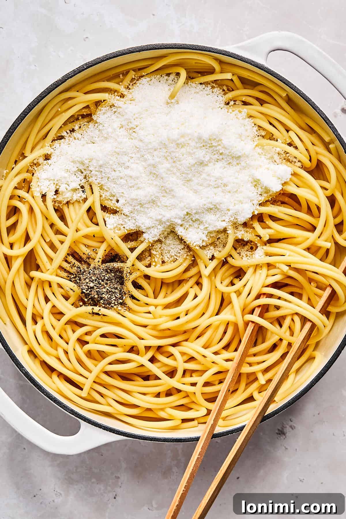 Stirring pecorino romano and black pepper into hot pasta in skillet
