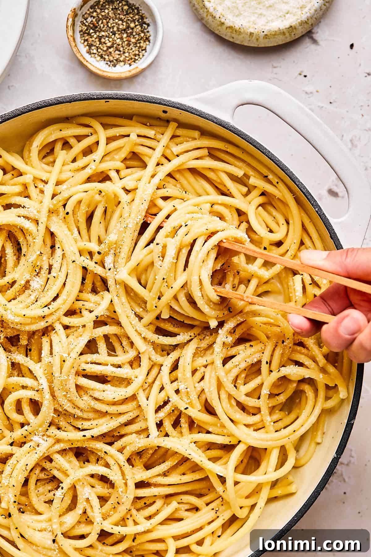 Close-up of bucatini cacio e pepe twirled on tongs with cracked pepper and grated cheese