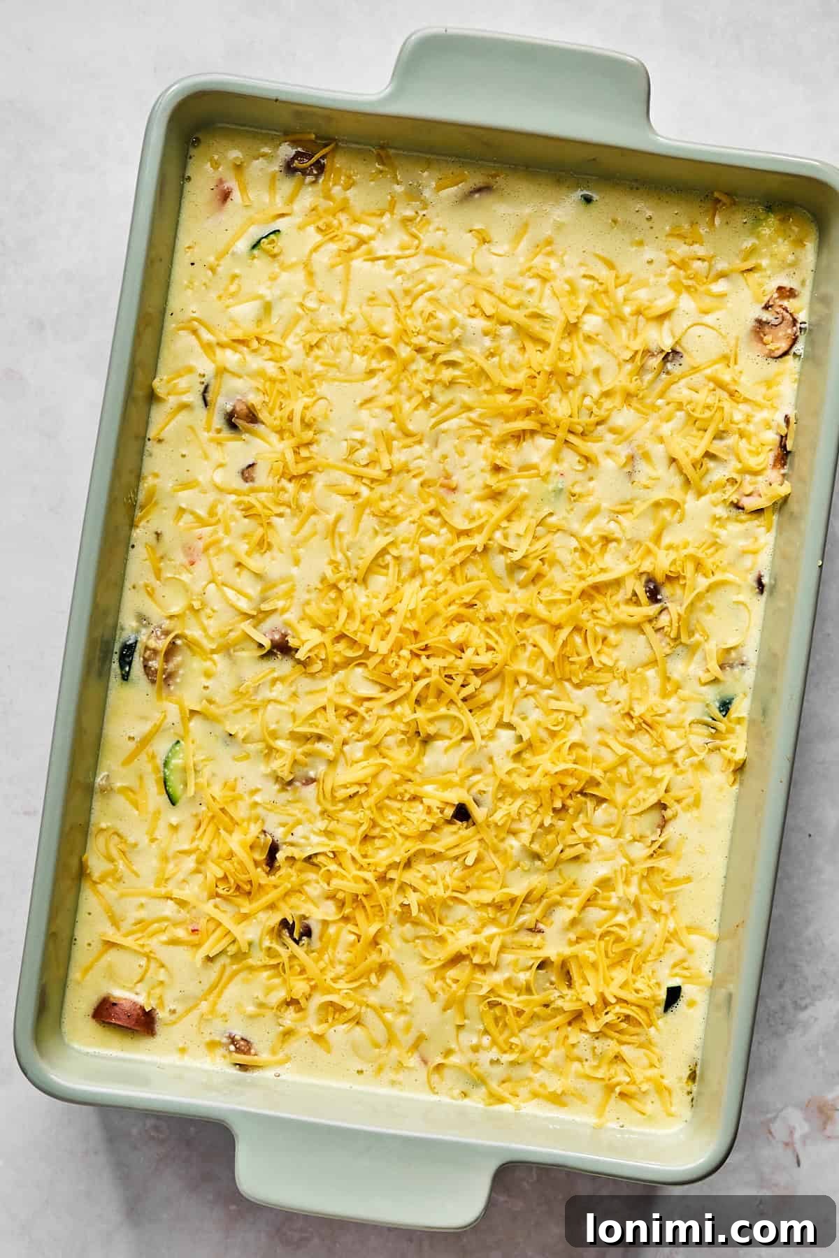 Unbaked egg casserole sprinkled with cheddar cheese, ready to go into the oven