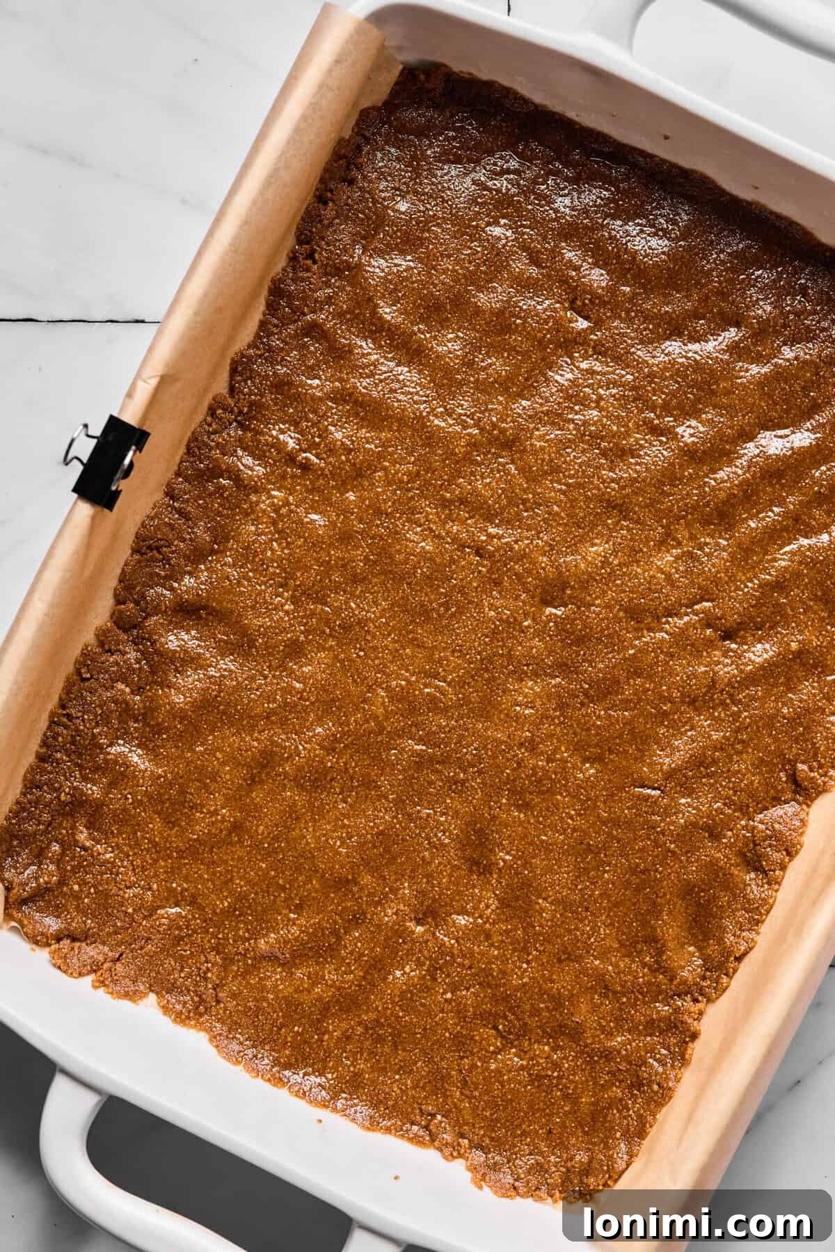Pressed Sweet Thins crust evenly packed into parchment-lined baking dish, forming a smooth, compact base.