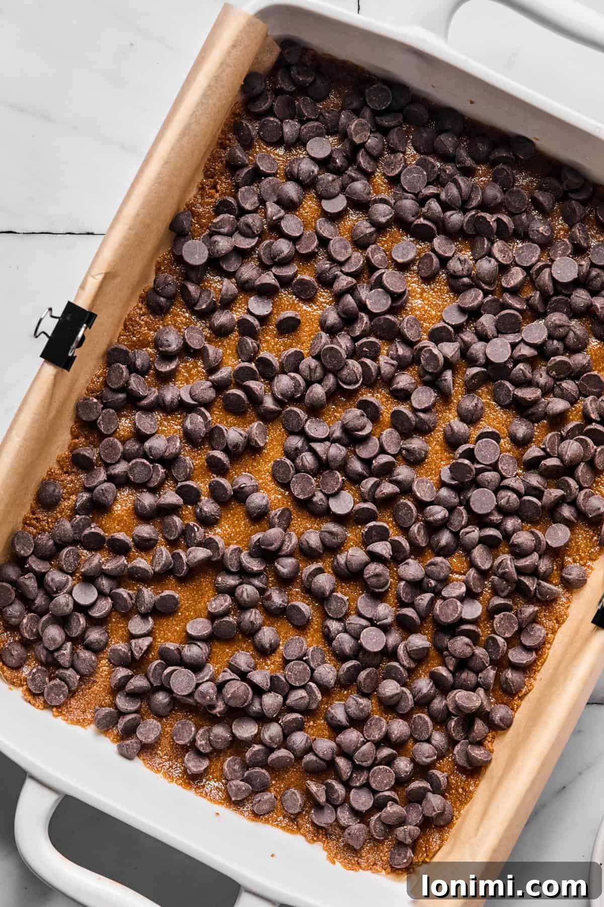 Dark chocolate chips layered over gluten-free crust in baking pan, forming the first topping layer.