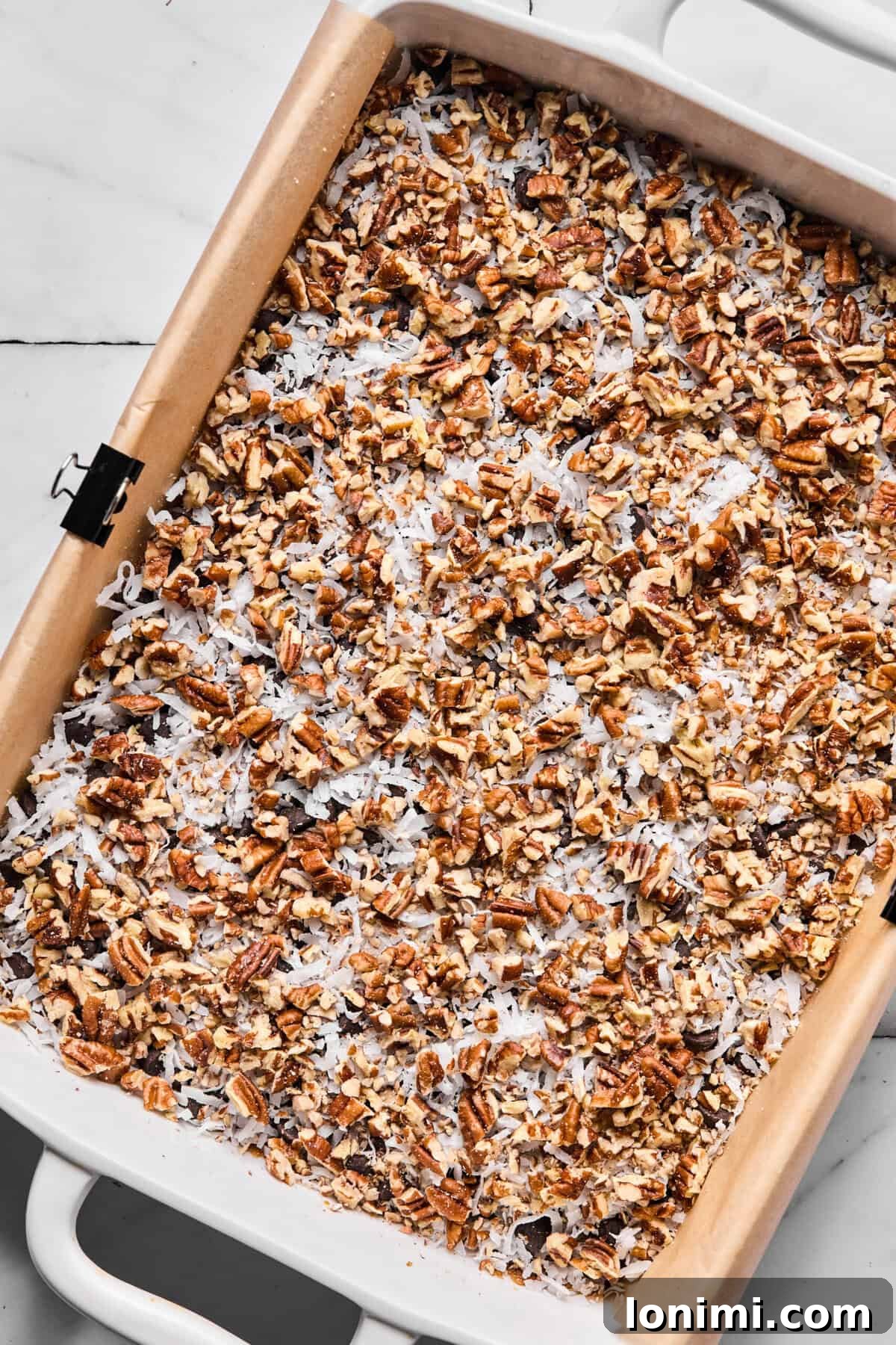 Chopped pecans and coconut flakes sprinkled over chocolate chip layer, creating a diverse topping.