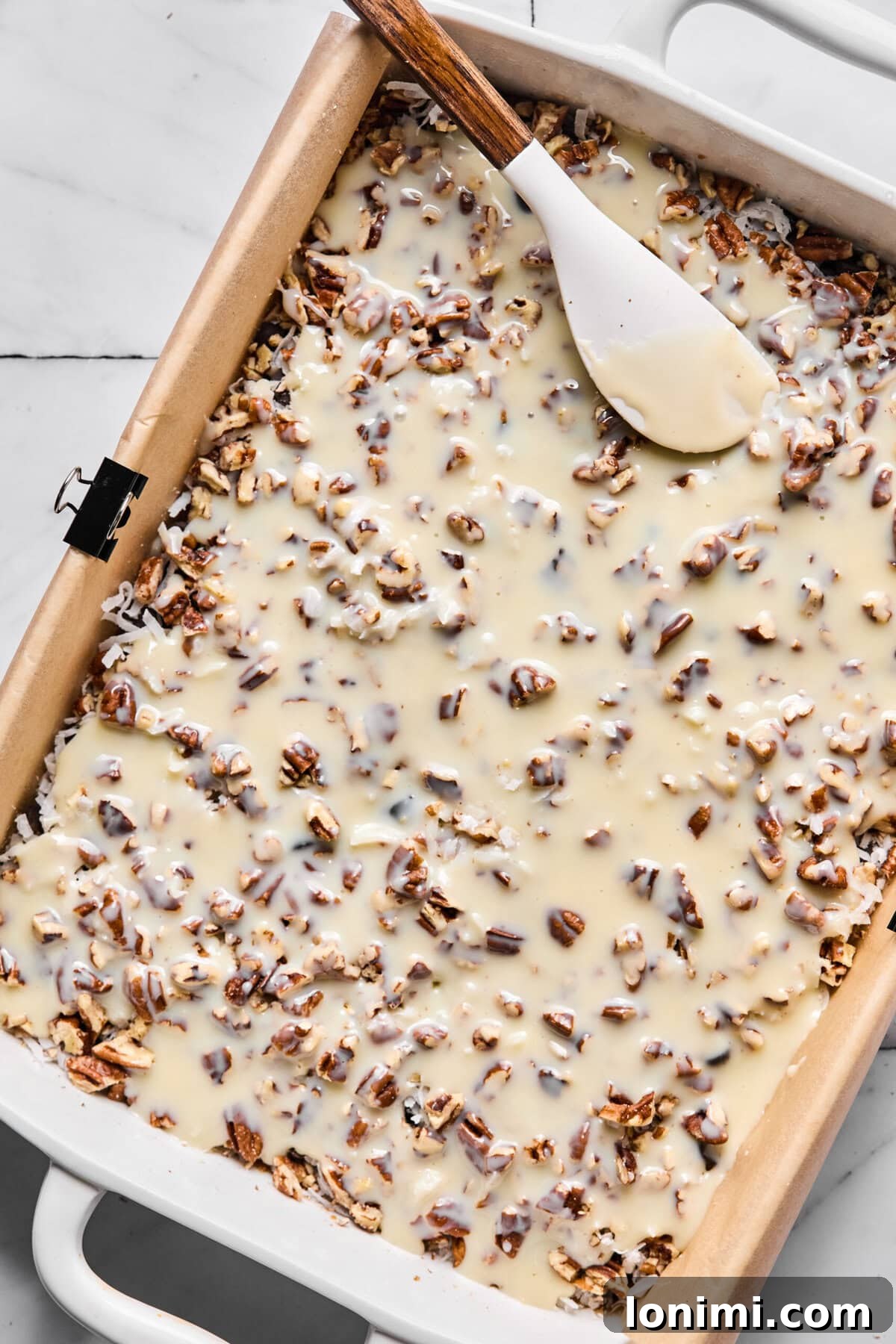Sweetened condensed milk poured evenly over layered ingredients, showcasing the binding step.