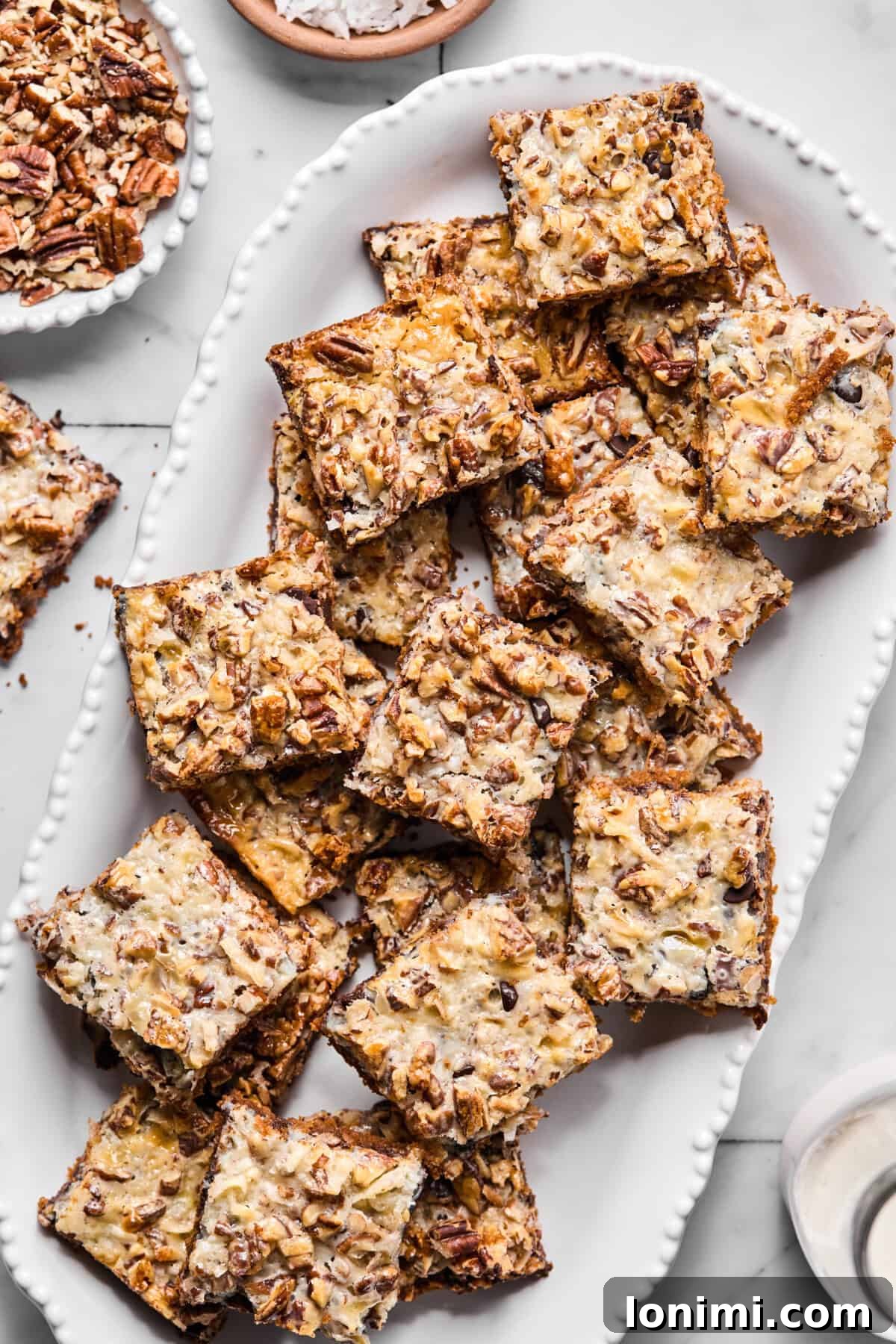 A serving platter filled with perfectly cut gluten-free magic bar squares, showing the tops with visible chocolate, coconut, nuts, and a golden condensed milk sheen.