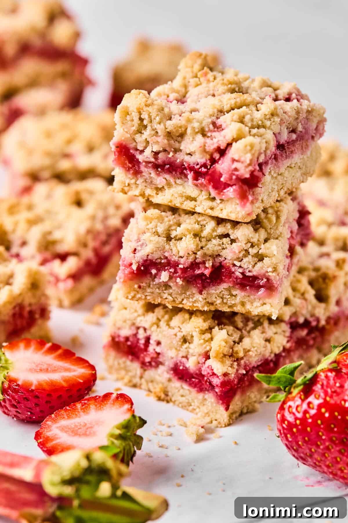 Close-up of a stack of gluten-free strawberry rhubarb crumble bars showing jammy fruit filling and golden crumble topping