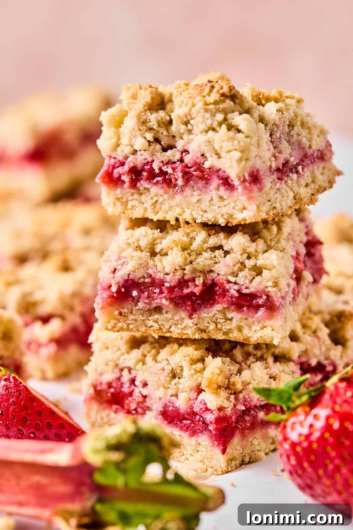 stack of of strawberry rhubarb crumble bars on a counter, showcasing jammy center and crumbly top