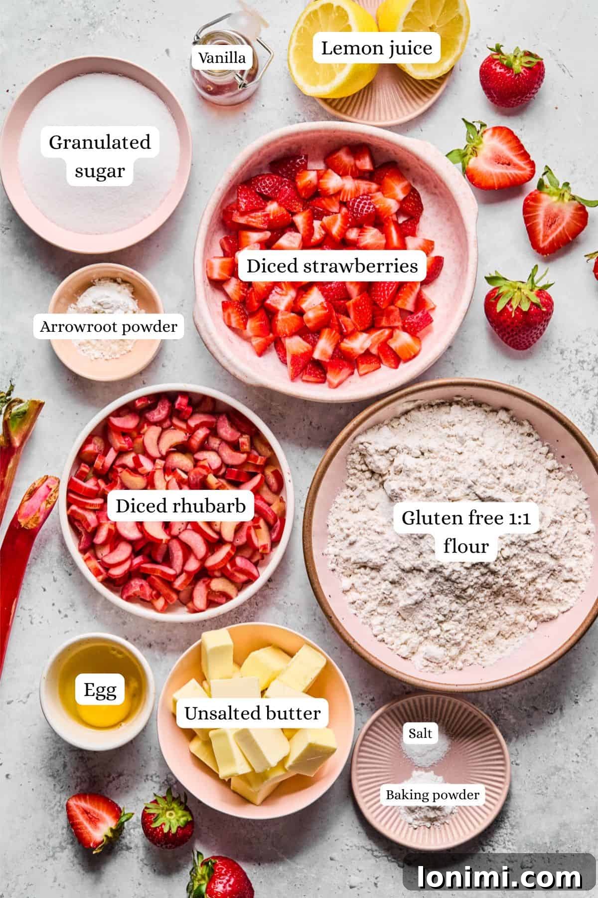 Overhead shot of ingredients laid out for strawberry rhubarb bars: fresh strawberries, rhubarb, arrowroot powder, gluten-free flour blend, cubed butter, egg, sugar, baking powder, salt, and vanilla