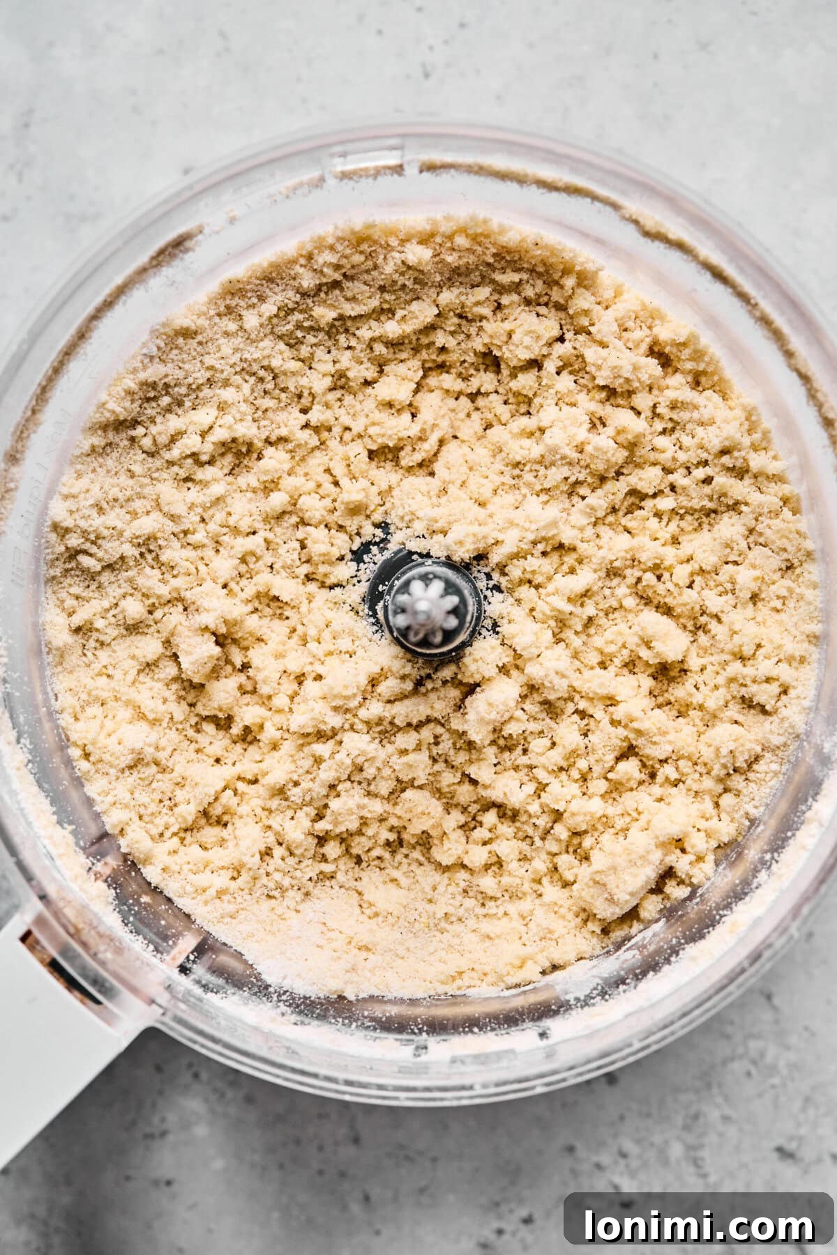 Food processor bowl filled with pea-sized crumbs of gluten-free crumble dough