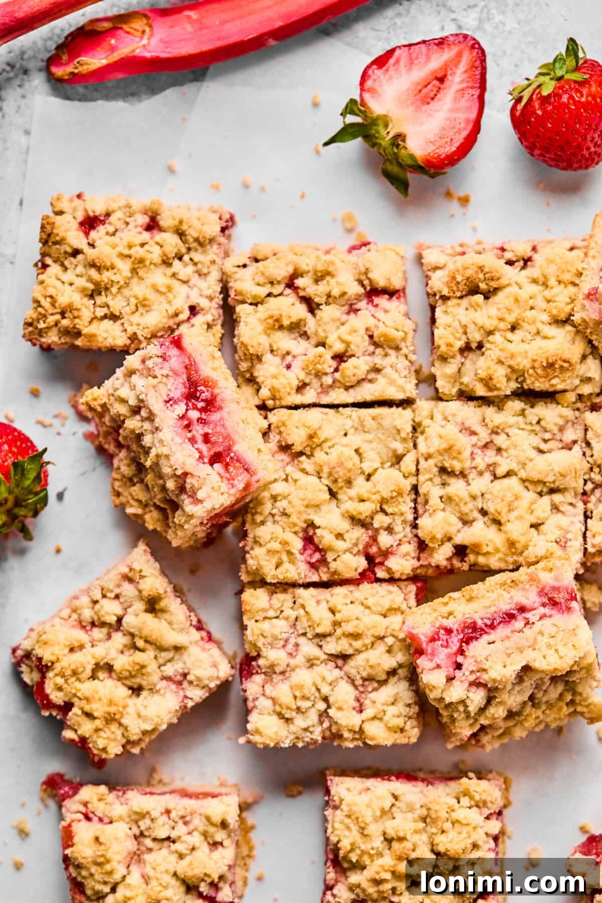 Freshly baked strawberry rhubarb crumble bars cooling on a counter, with bubbling fruit peeking through golden topping