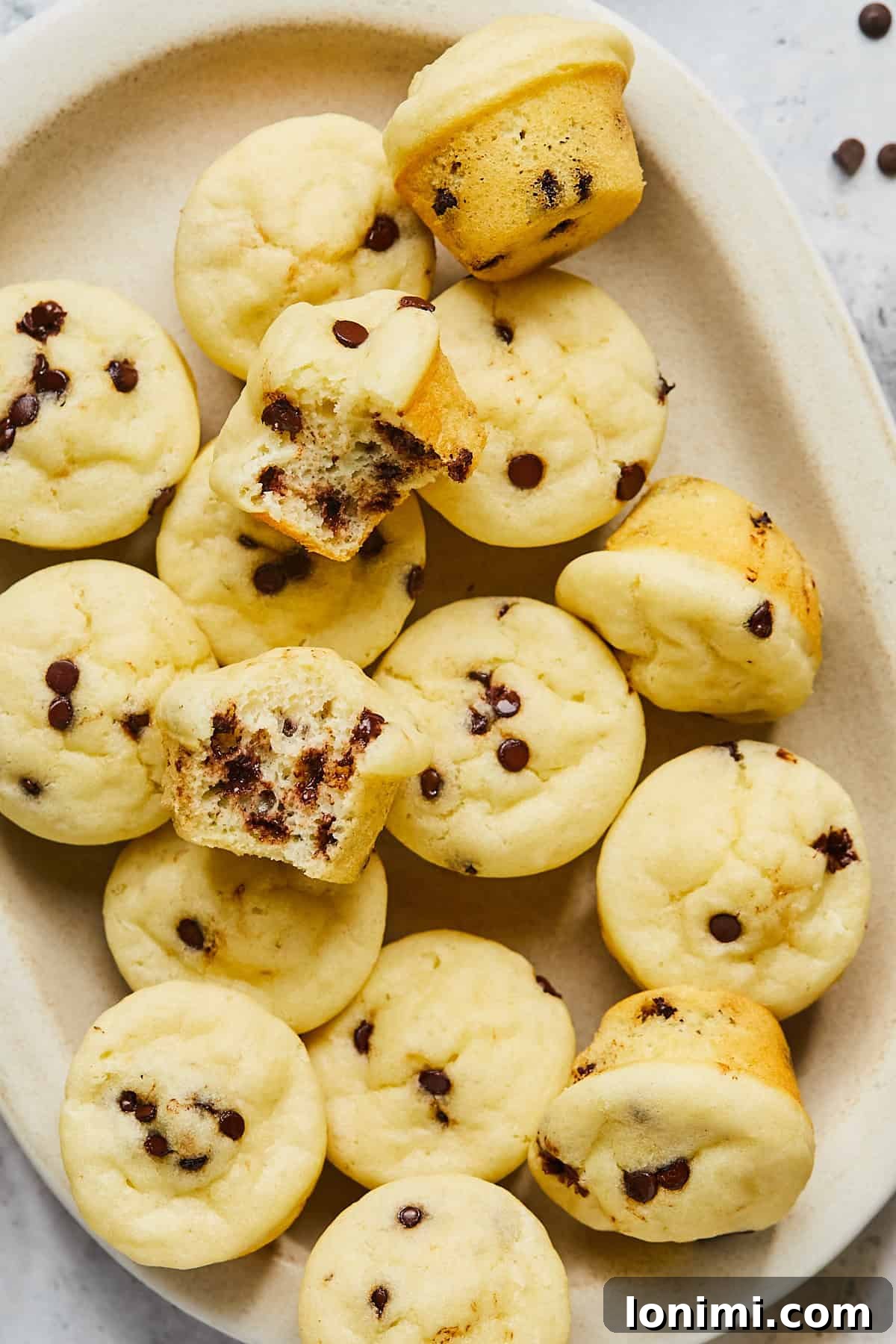 A tray of golden-brown gluten-free mini muffins, with one cut in half to reveal its incredibly fluffy, moist interior.