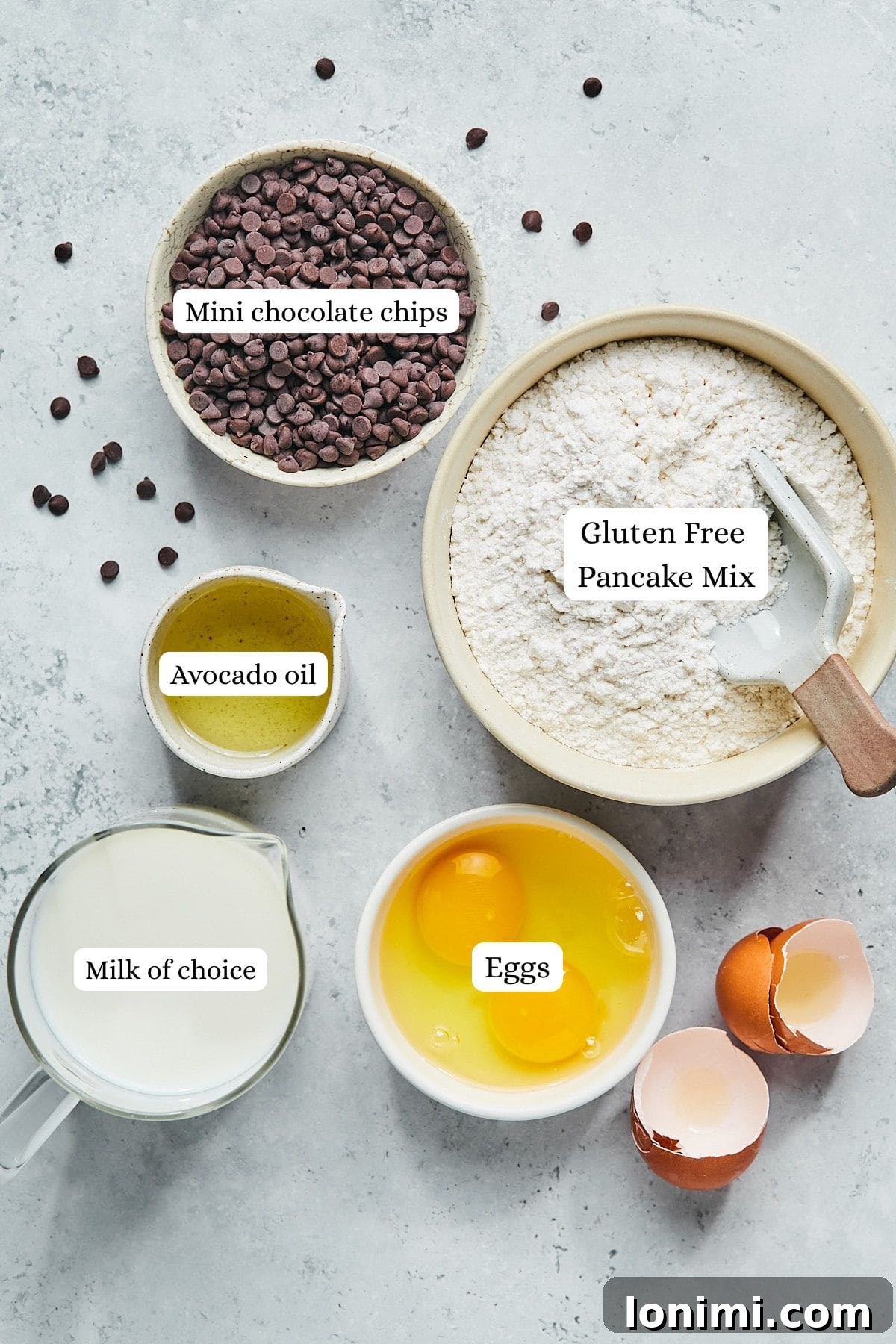 A visual display of the five simple ingredients required for gluten-free mini muffins: gluten-free pancake mix, almond milk, eggs, avocado oil, and mini chocolate chips, neatly arranged on a countertop.