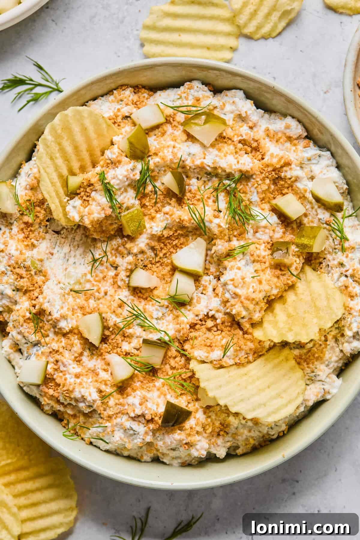 Vibrant Fried Pickle Dip in a light green bowl, artfully surrounded by an array of crispy potato chips ready for scooping. Perfect for parties and snacking.