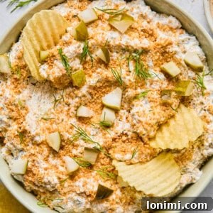 Vibrant Fried Pickle Dip in a light green bowl, artfully surrounded by an array of crispy potato chips ready for scooping. Perfect for parties and snacking.