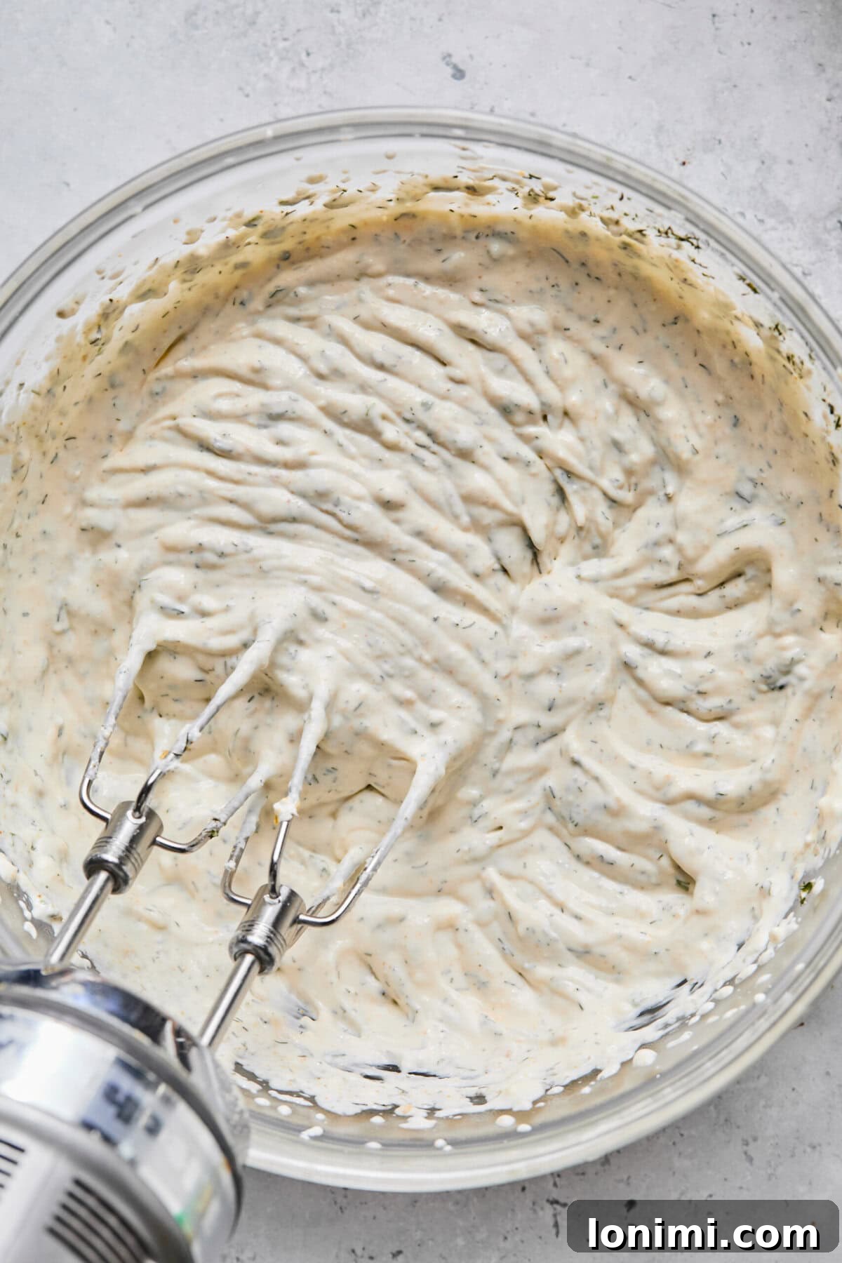 A creamy mixture for pickle dip being smoothly blended in a white bowl with an electric mixer, creating a luscious and consistent texture.