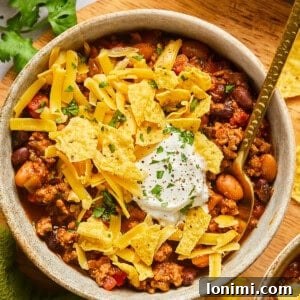 taco chili in a bowl topped with crushed chips, sour cream, and cheese