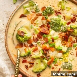 loaded broccoli cheese & potato soup in a bowl with a spoon taking a bite out