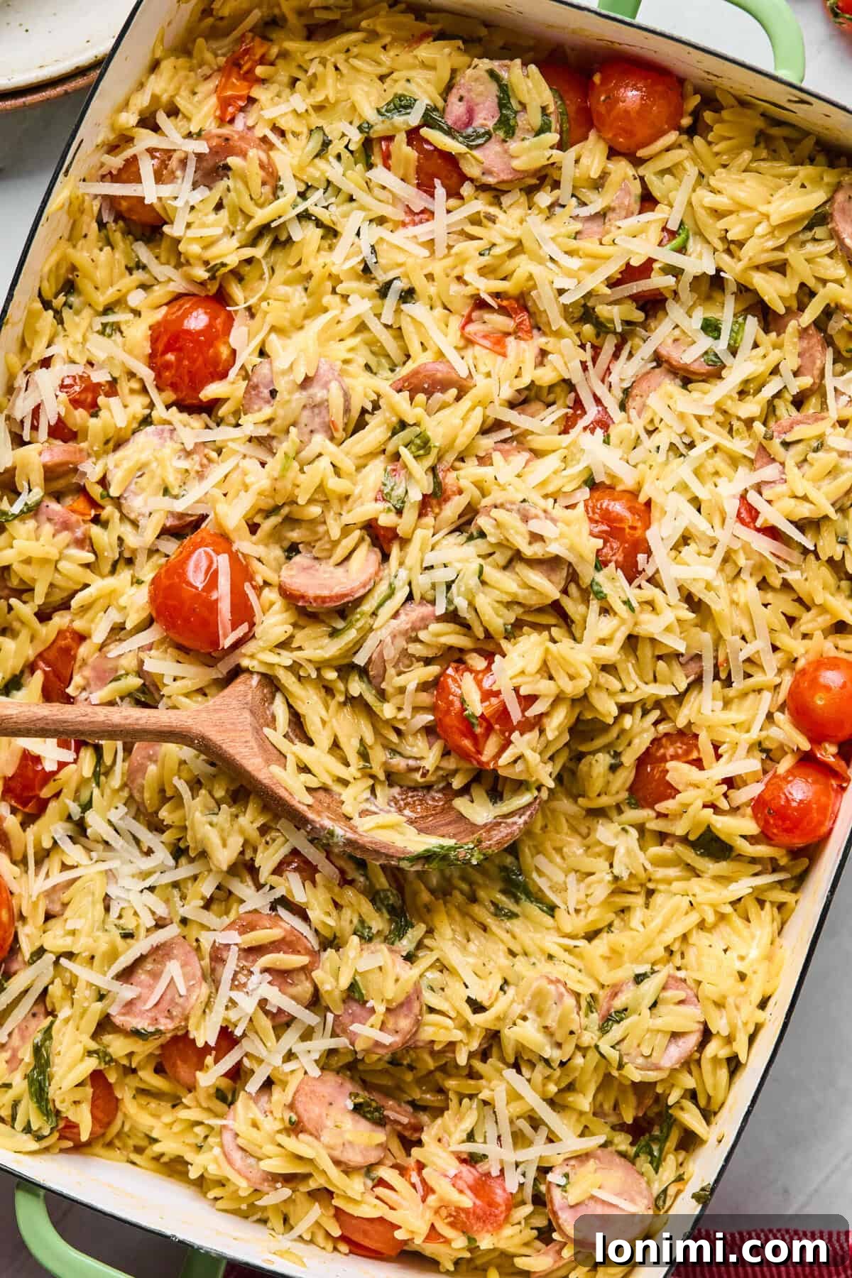Baked one pan orzo with chicken sausage, cherry tomatoes, and spinach in a white baking dish.