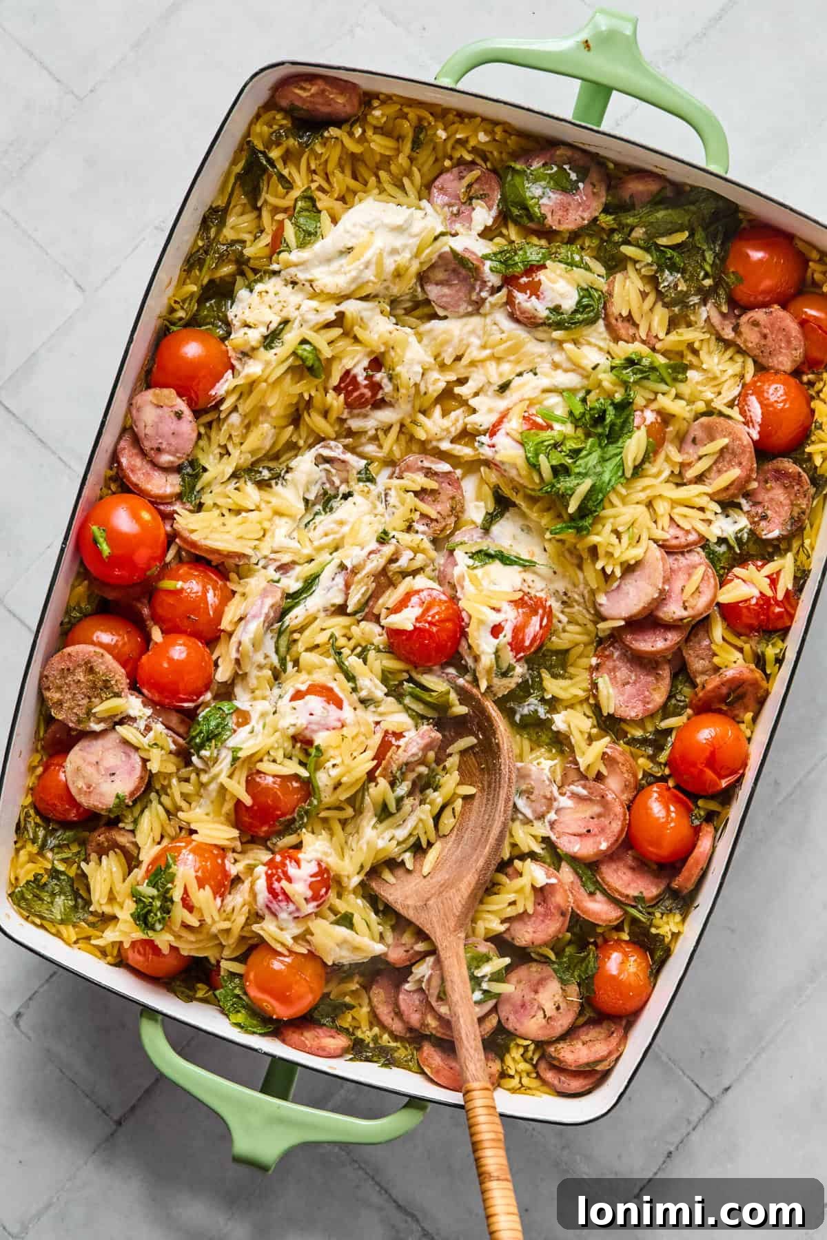 One pan orzo bake fresh out of the oven being stirred to create a creamy sauce.