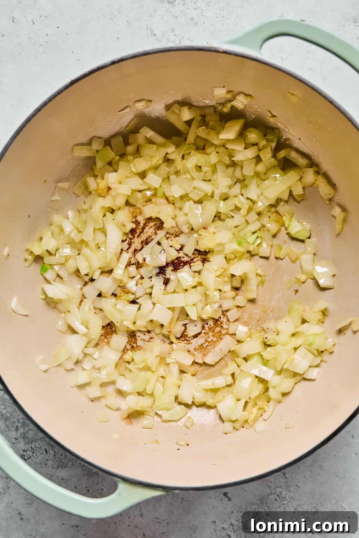 Sautéing diced onion and minced garlic in sausage drippings in a pot.