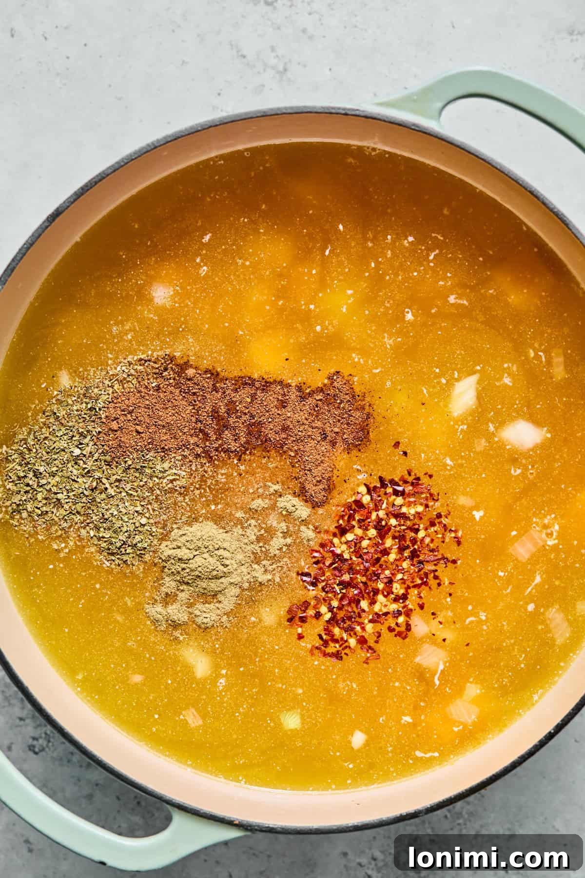 Cooking butternut squash cubes and seasonings in a pot of simmering chicken broth.